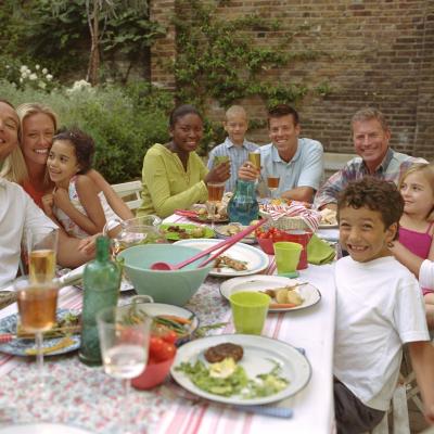 Diverse group of smiling families sitting around a dining table full of food. They are eating a meal together.